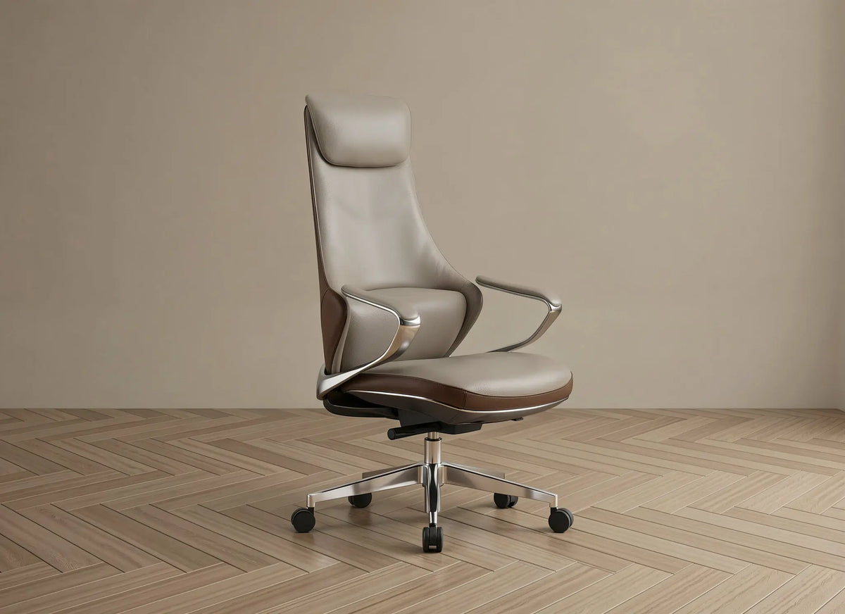 A modern high-back office chair upholstered in light taupe leather with dark brown leather trim, featuring chrome armrests and a five-star metal base with black casters, set against a minimalist beige wall and light wood herringbone floor.