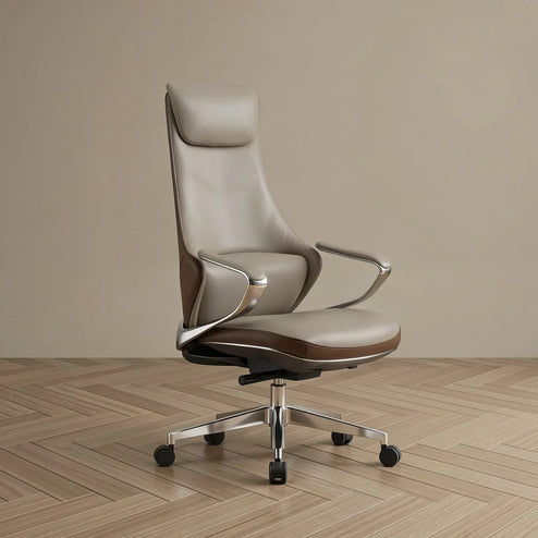 A modern high-back office chair upholstered in light taupe leather with dark brown leather trim, featuring chrome armrests and a five-star metal base with black casters, set against a minimalist beige wall and light wood herringbone floor.