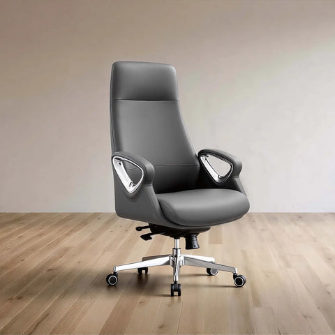 A modern gray leather office chair with a high back, curved armrests, and a chrome five-star base with casters, set against a minimalist beige wall and light wood floor.