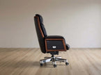 A high-back executive office chair with black leather upholstery and brown wood trim, mounted on a chrome five-star wheeled base, shown in profile against a neutral beige wall and light wood floor.