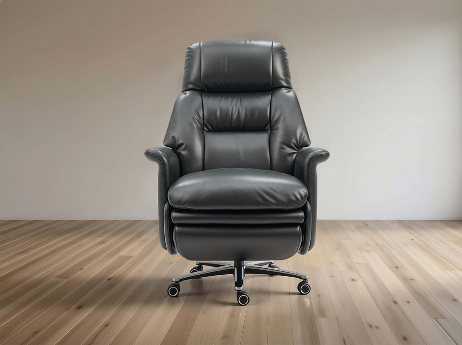 A dark gray leather office chair with a high back, padded armrests, and a chrome five-star rolling base, set against a minimalist beige wall and light wood floor.