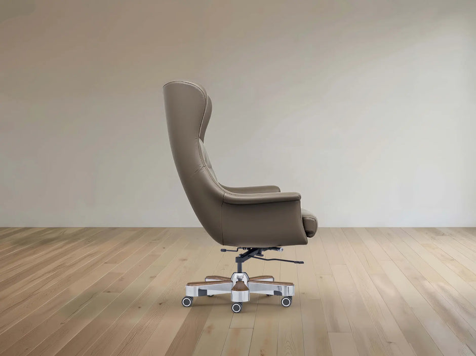 A modern high-back lounge chair upholstered in taupe leather, shown from the side on a light-colored wooden floor against a neutral beige wall.
