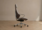 A modern high-back office chair with a brown and white upholstered seat and back, supported by a chrome metal frame and five-star wheeled base, set against a minimalist beige wall and light wood herringbone floor.