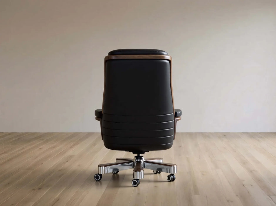 A black leather office chair with a high back, silver five-star base, and wood trim, shown from the rear on a light wood floor against a neutral beige wall.