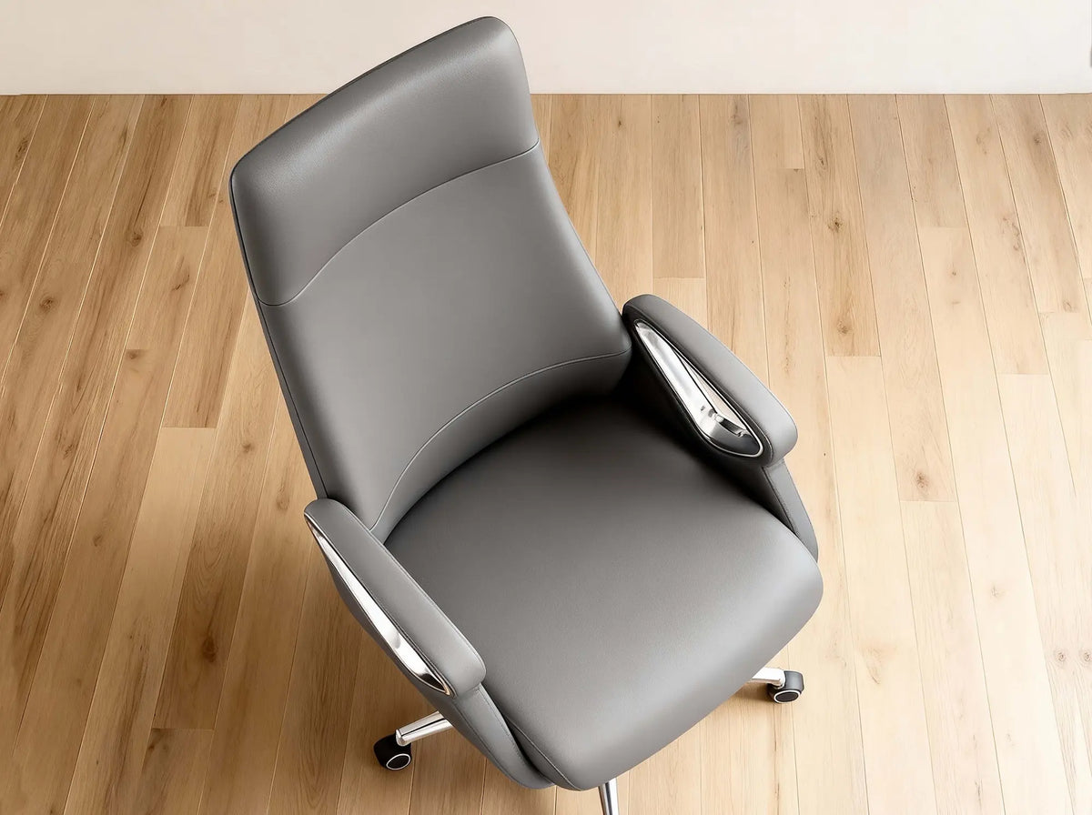 A gray upholstered office chair with chrome armrest accents and a five-wheel base, photographed from above on a light wood floor against a white wall.