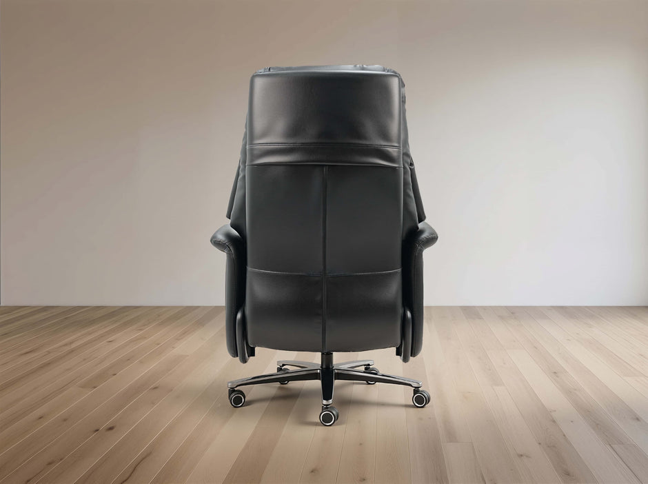A black leather office chair with a high back and five-wheel base, shown from the rear in a minimalist room with light wood floors and a beige wall.