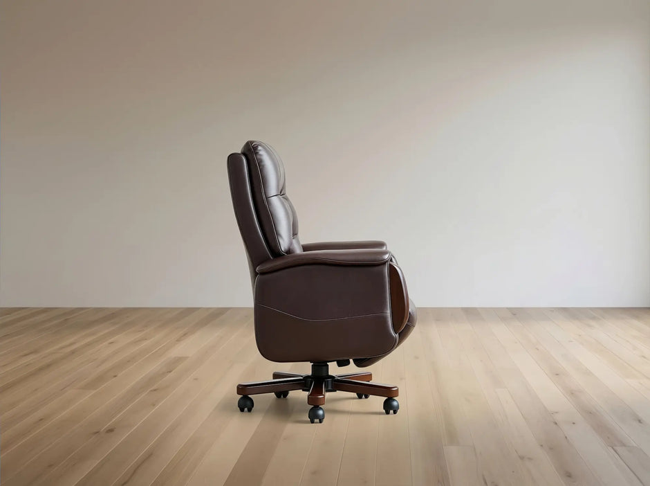 A dark brown leather office chair with a high back and five-star wheeled base, shown in profile on a light wood floor against a neutral beige wall.