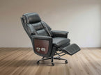 Black leather recliner office chair with extended footrest and wood-grain side panel, shown on a light wood floor against a neutral beige wall.
