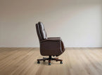 A dark brown leather office chair with a high back and five-star wheeled base, shown in profile on a light wood floor against a neutral beige wall.