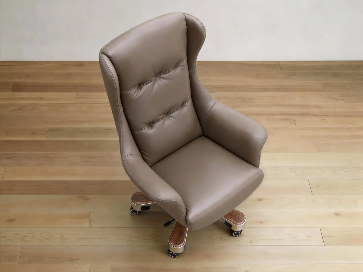 A high-back wingback office chair upholstered in taupe leather with tufted button detailing on the backrest, shown on a light wood floor against a neutral wall.