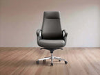 A dark gray leather office chair with a high back, silver armrest supports, and a chrome five-star wheeled base, set against a minimalist beige wall and light wood floor.