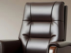 A close-up of a dark brown leather recliner chair with padded segmented backrest and armrests, shown against a plain beige studio background.