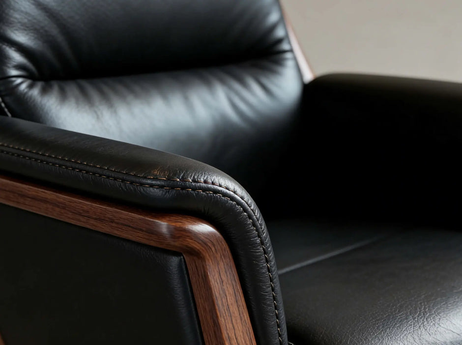 Close-up of a black leather armchair with a polished dark wood armrest frame, showing the texture of the leather and the wood grain.