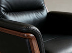 Close-up of a black leather armchair with a polished dark wood armrest frame, showing the texture of the leather and the wood grain.