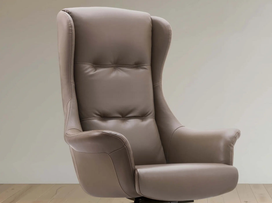 A high-back wingback office chair upholstered in taupe leather, shown from a three-quarter angle against a neutral beige wall and light wood floor.