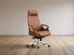 A brown leather high-back office chair with silver armrest supports and a chrome five-star wheeled base, set against a minimalist beige wall and light wood floor.