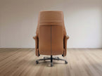 A tan leather office chair with a high back and five-star wheeled base, photographed from the rear in a minimalist room with light wood flooring and a neutral wall.