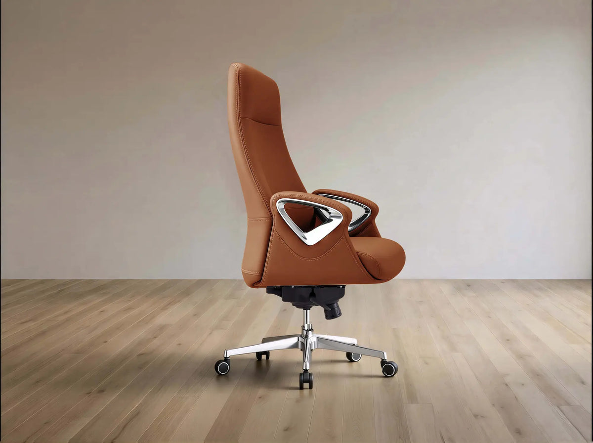 A modern high-back office chair upholstered in warm brown leather with a silver metal frame and five-wheel base, set against a minimalist beige wall and light wood floor.