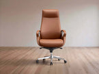 A high-back brown leather office chair with a chrome five-star base and casters, set against a minimalist beige wall and light wood floor.