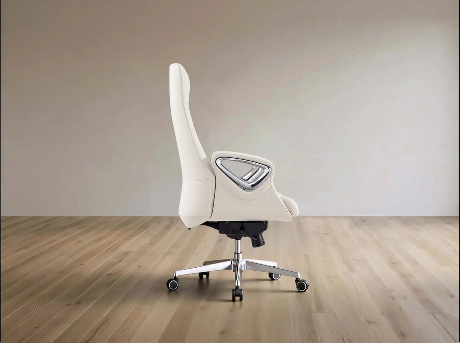 A modern white gaming chair with a high backrest, silver armrest frame, and chrome five-star wheeled base, shown in a minimalist room with light wood flooring and a beige wall.