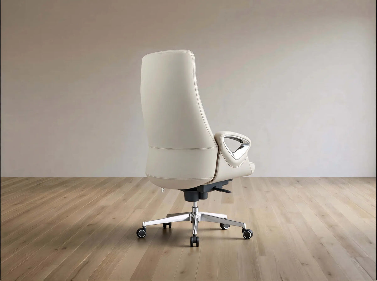 A modern off-white leather high-back office chair with a chrome five-star base and casters, shown from a three-quarters angle in a minimalist room with light wood floors and beige walls.