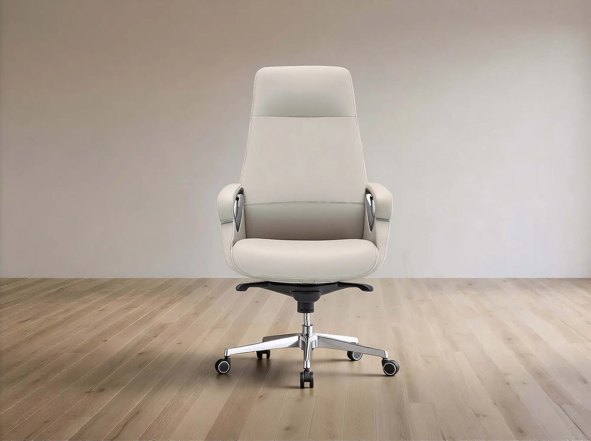 A modern high-back office chair upholstered in light beige leather, featuring chrome armrest supports and a five-star metal base with casters, set against a minimalist beige wall and light wood floor.