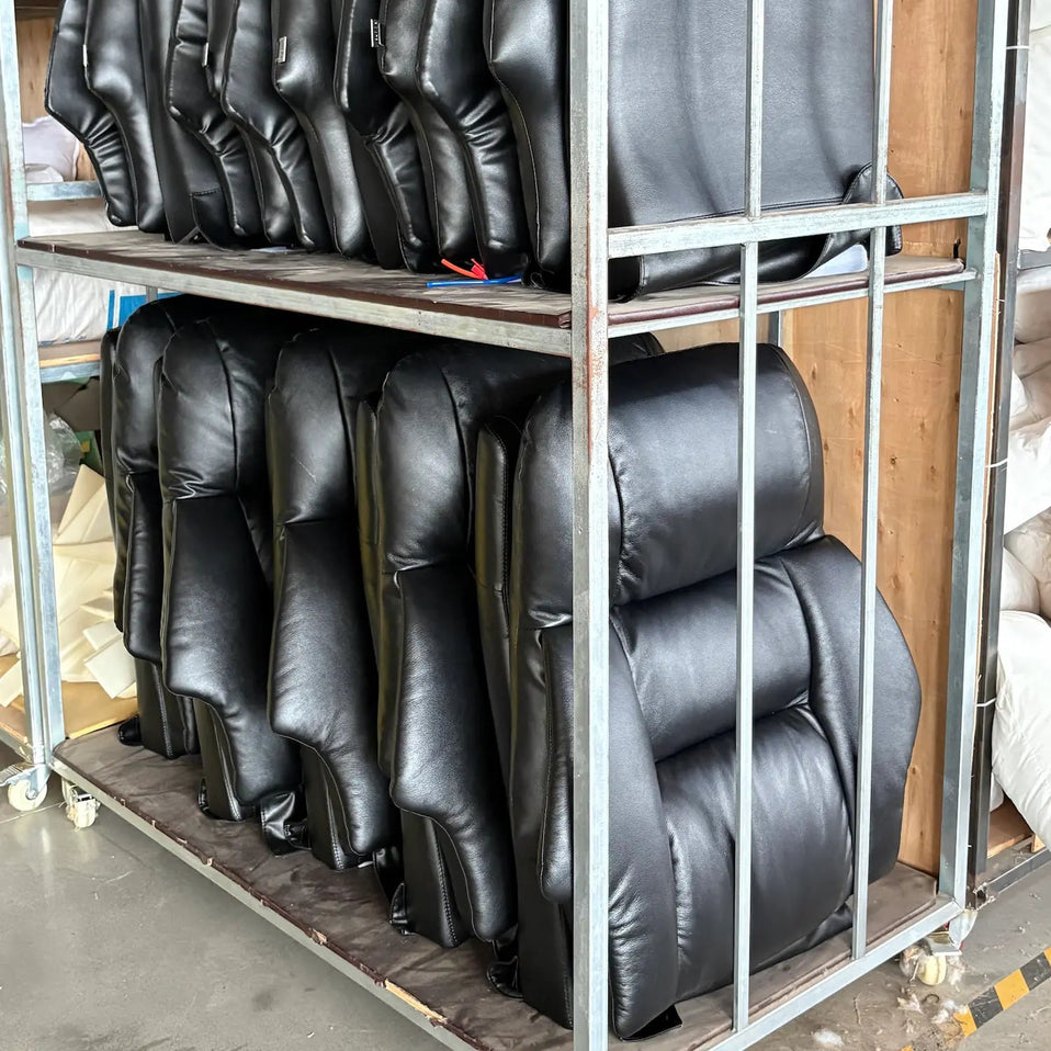 Several black leather or faux-leather chair backrests or upholstered seat cushions stacked on a metal shelving unit in a warehouse or workshop setting.