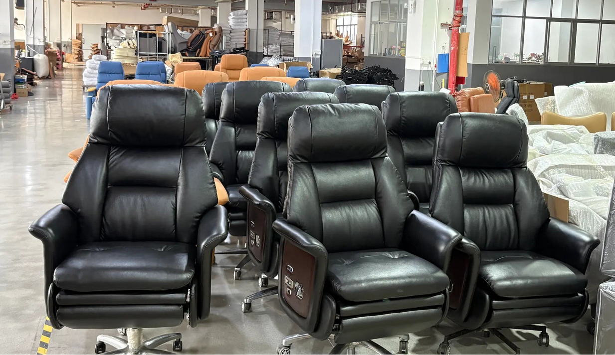 A group of black leather office chairs with adjustable headrests and armrests, some featuring dark wood side panels with control buttons, displayed in a warehouse showroom.
