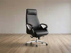 A modern black leather high-back office chair with chrome armrest supports and a five-star wheeled base, set against a minimalist beige wall and light wood floor.