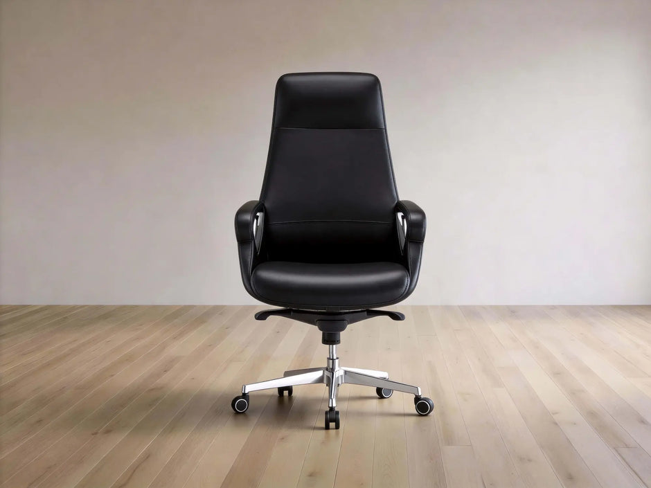 A black leather high-back office chair with a chrome five-star base and casters, set against a minimalist beige wall and light wood floor.