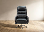 A black leather high-back office chair with a chrome five-star wheeled base, set against a minimalist beige wall and light wood floor.