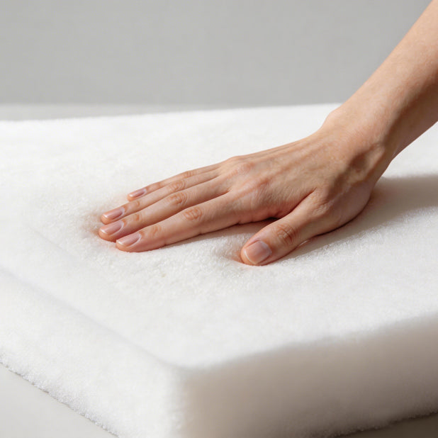 Hand touching a white mattress to check its softness on a light gray background